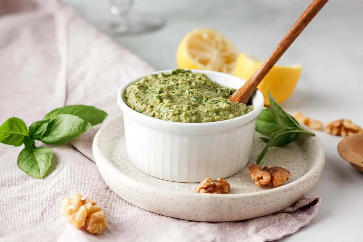 vegan basil pesto with walnuts in bowl with ingredients surrounding pesto