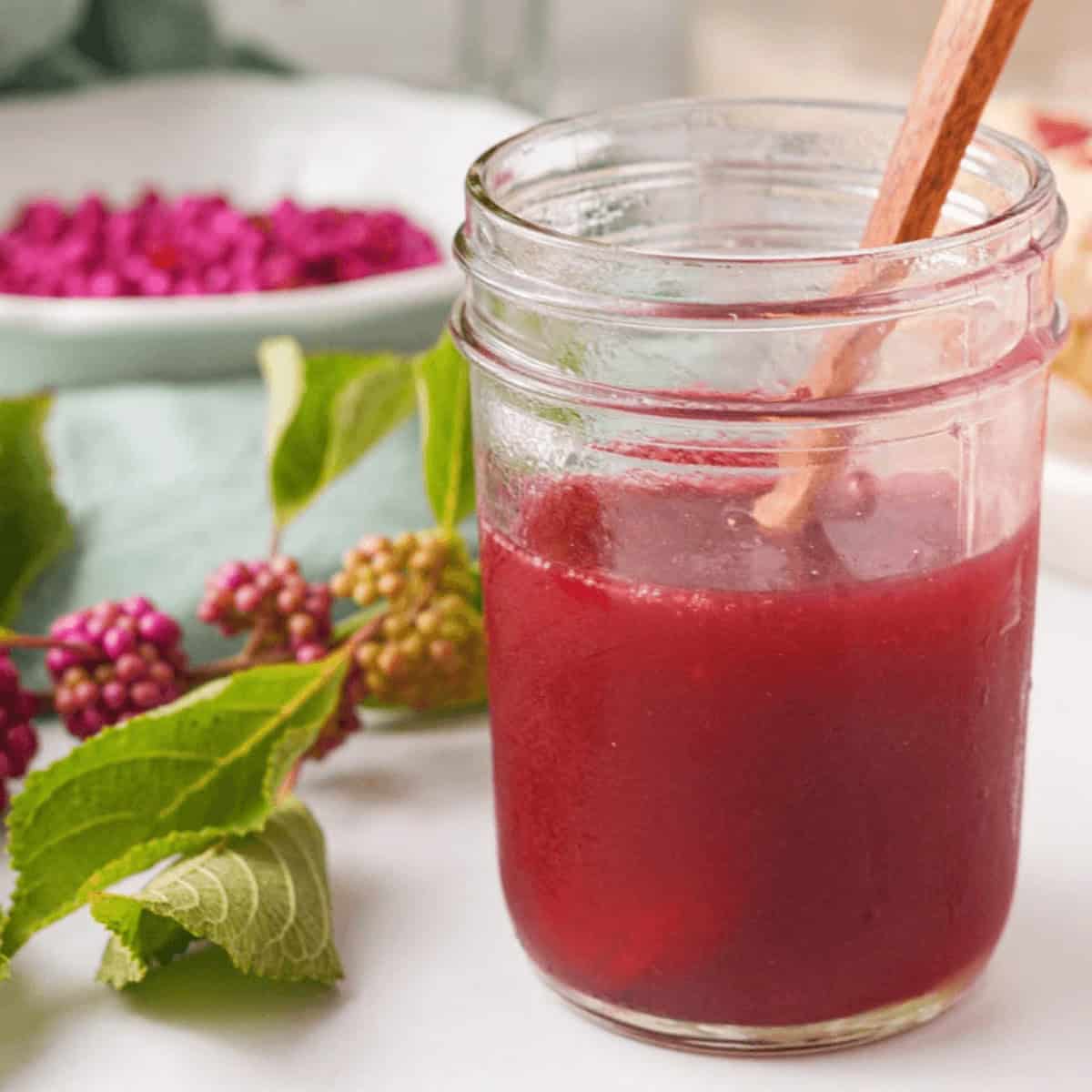 closeup of beautyberry jelly in jar with branch and loose berries in background