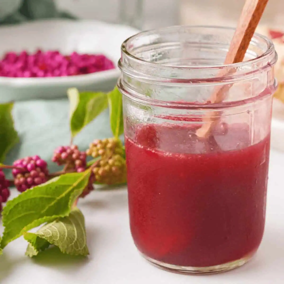 closeup of beautyberry jelly in jar with branch and loose berries in background