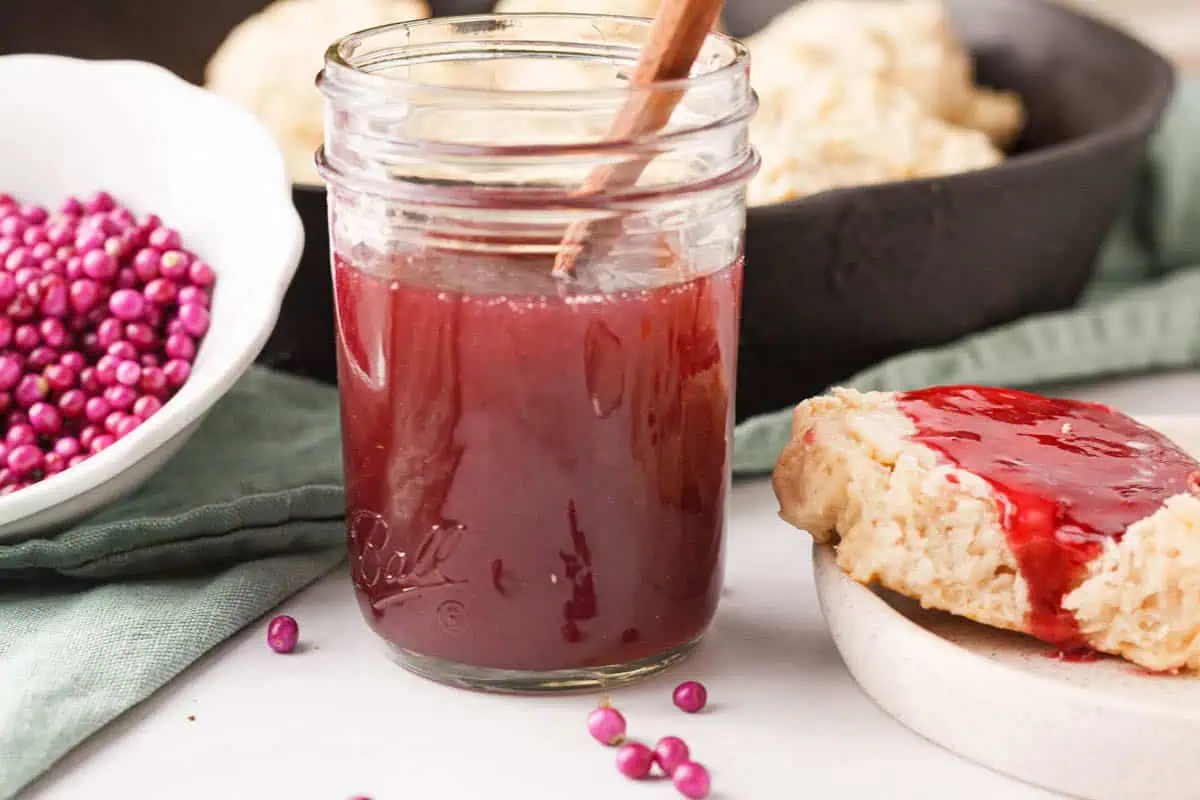 closeup of beautyberry jelly in jar next to a bowl of berries and a biscuit with jelly spread on top