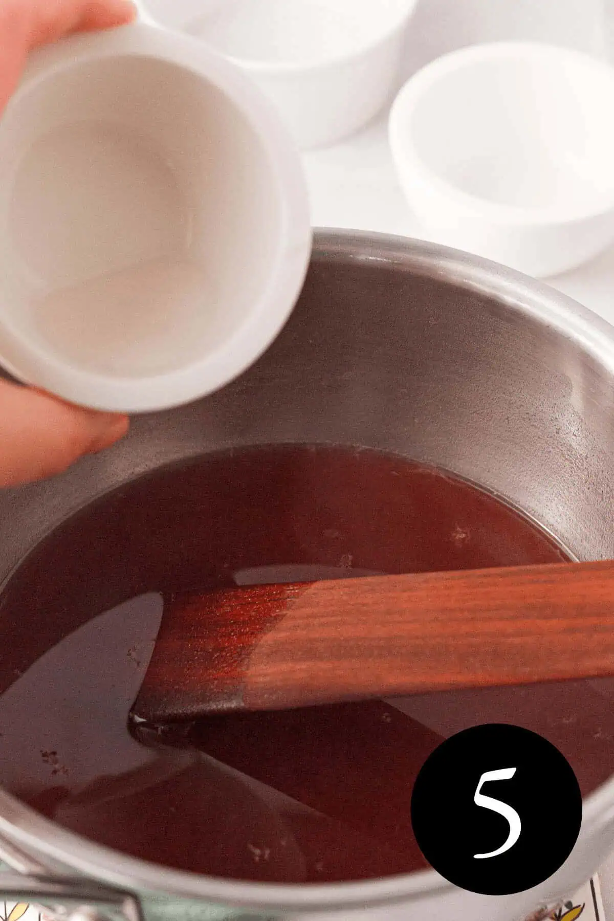 angled image of hand pouring arrowroot powder slurry into beautyberry liquid and number five in the bottom right corner
