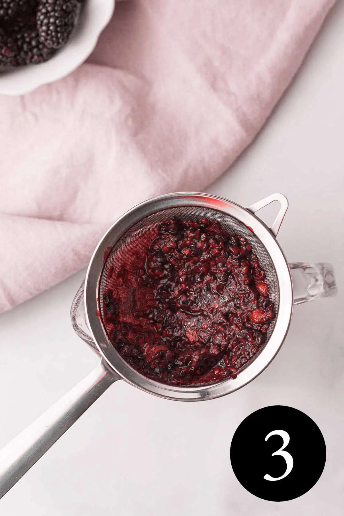 overhead image of blackberry pulp in strainer and number three in the bottom right corner