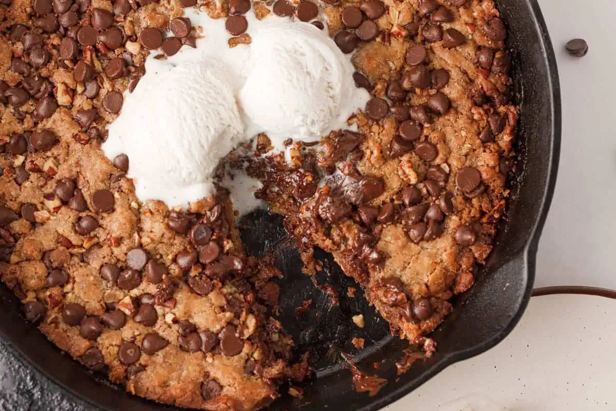 overhead image of vegan skillet cookie cake with slice removed and ice cream melting into the void