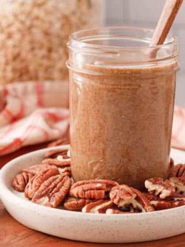 square image of pecan butter in jar surrounded by loose pecan halves