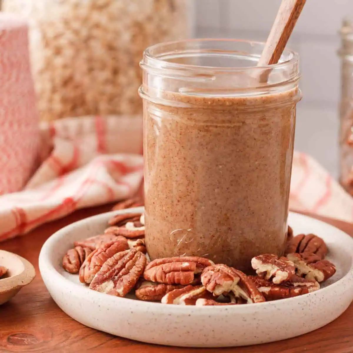 square image of pecan butter in jar surrounded by loose pecan halves