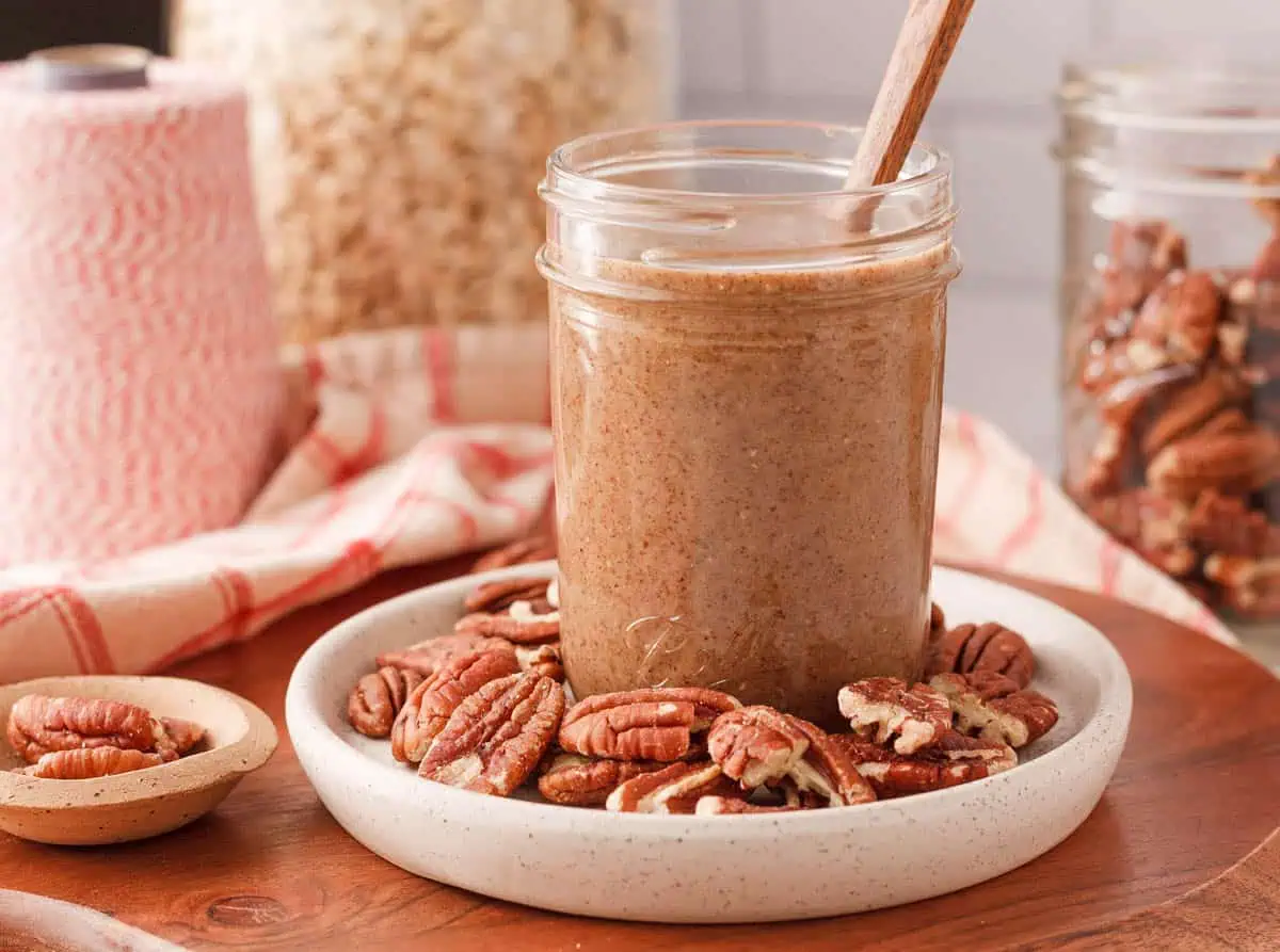 pecan butter in jar surrounded by pecan halves and ingredients in the background