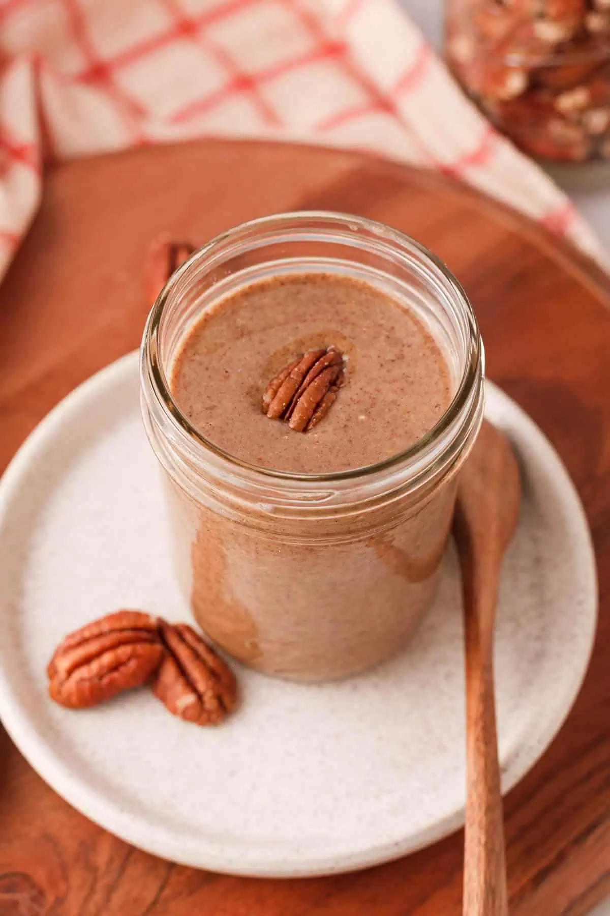 angled image of pecan butter with pecan half resting on top of the nut butter in the jar