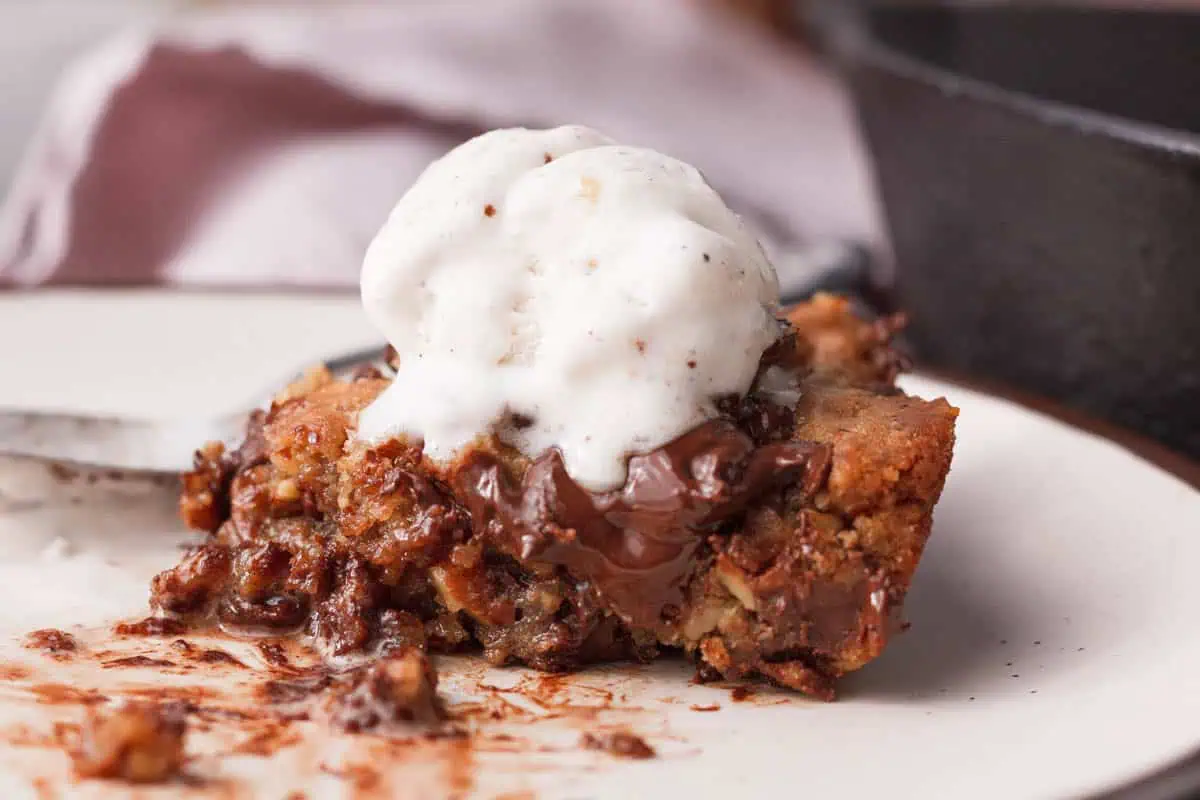 closeup of a cast iron skillet cookie cake slice on plate topped with ice cream
