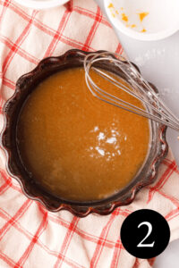 overhead image of pumpkin icing glaze in bowl with whisk propped on the side and number two in the bottom right corner