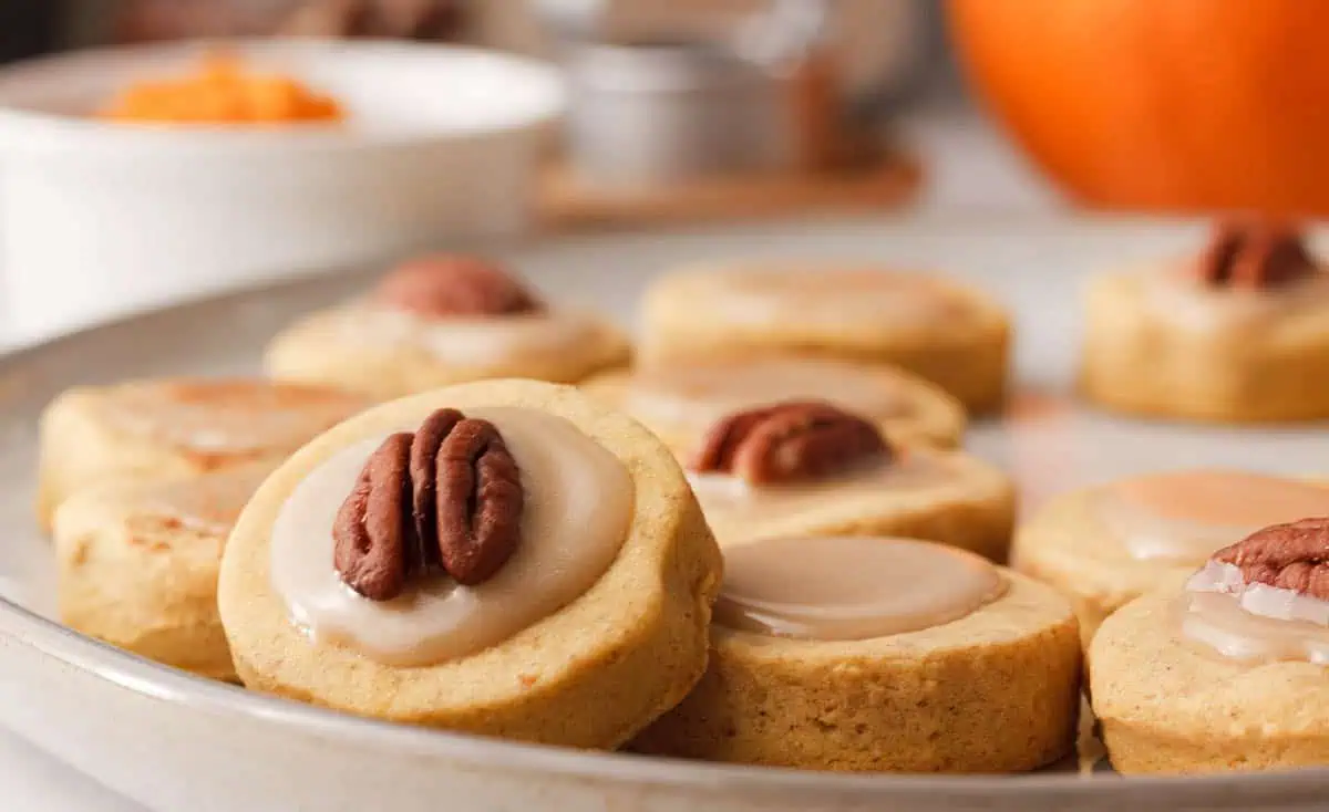 closeup of pumpkin shortbread cookies on plate with a cookie propped to show topping