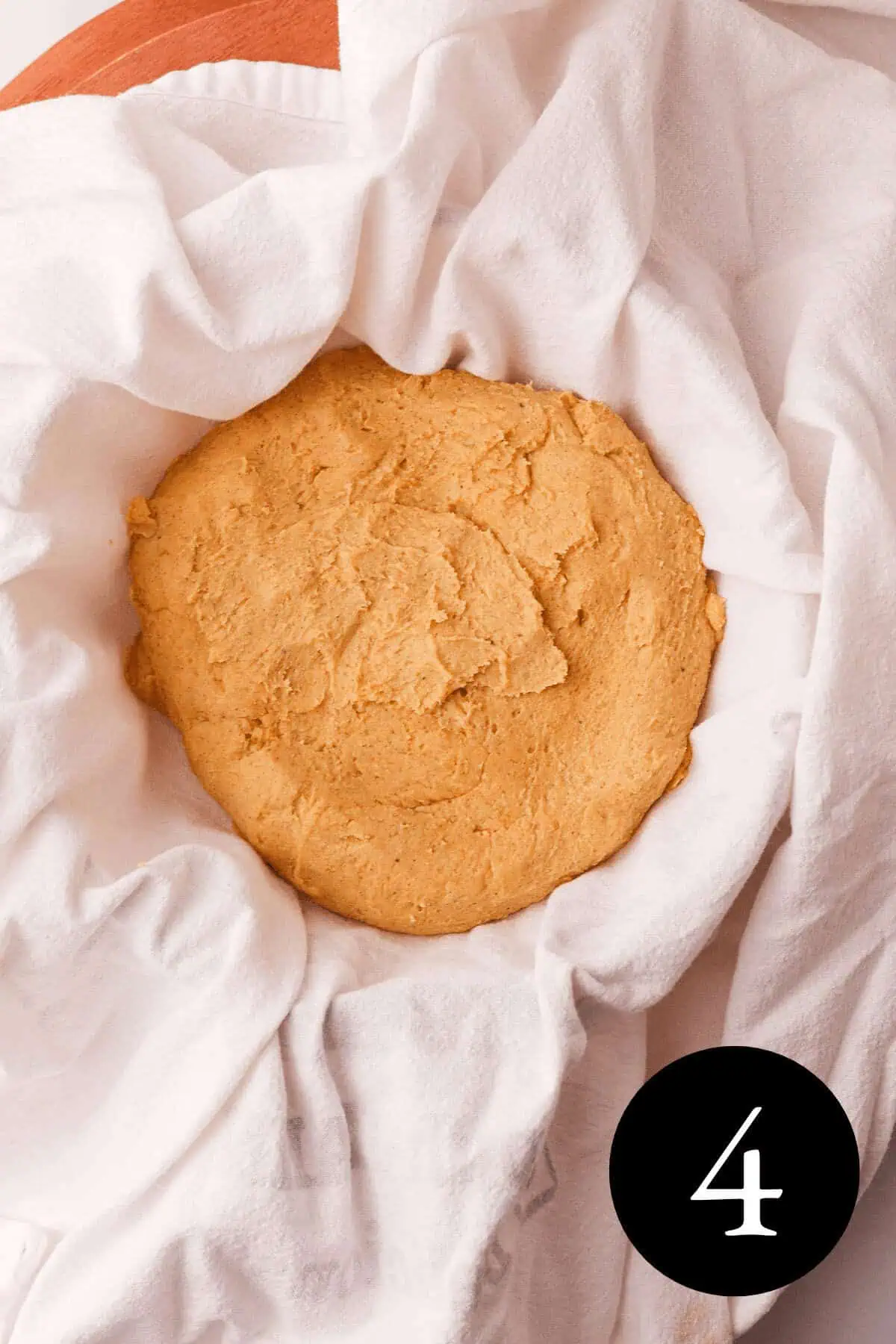 overhead image of pumpkin shortbread dough pressed into a disc shape and sitting in a bowl lined with a cotton tea towel and number four in bottom right corner