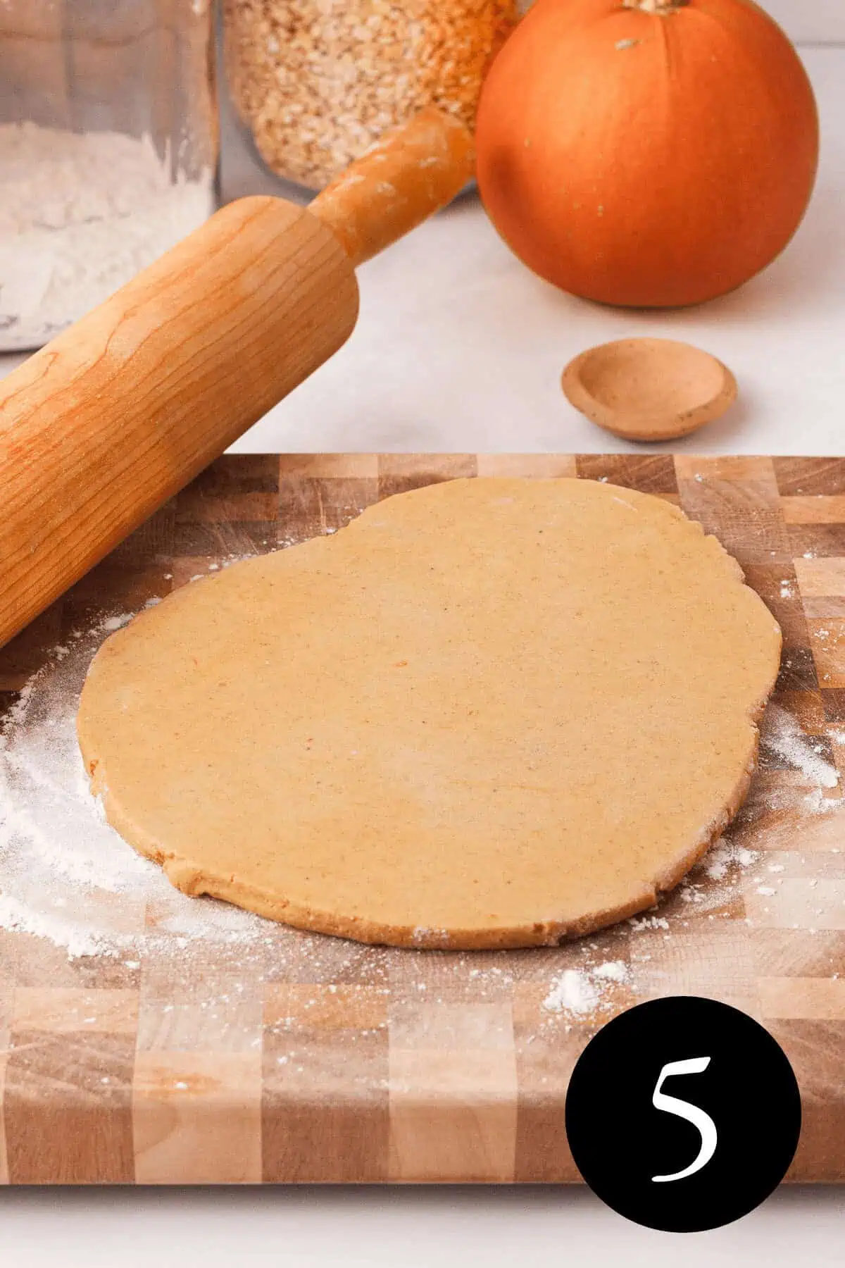 angled image of pumpkin shortbread dough rolled out on cutting board next to rolling pin and number five in the bottom right corner