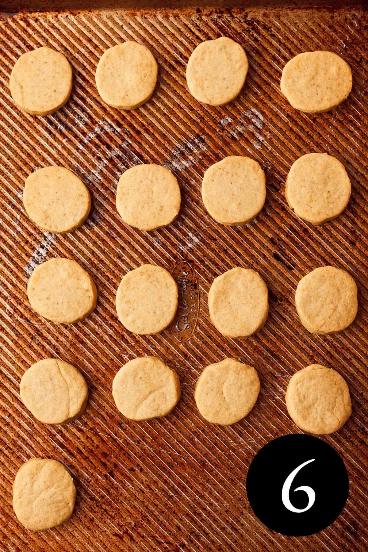 overhead image of baked pumpkin shortbread cookies on baking sheet with number six in the bottom right corner
