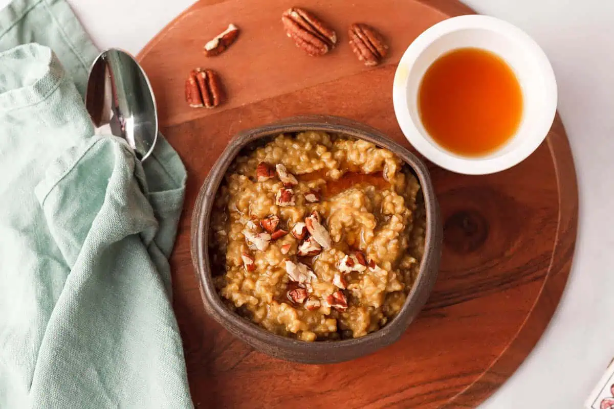 overhead image of pumpkin steel cut oats in bowl with spoon, maple syrup, and pecans accenting the bowl