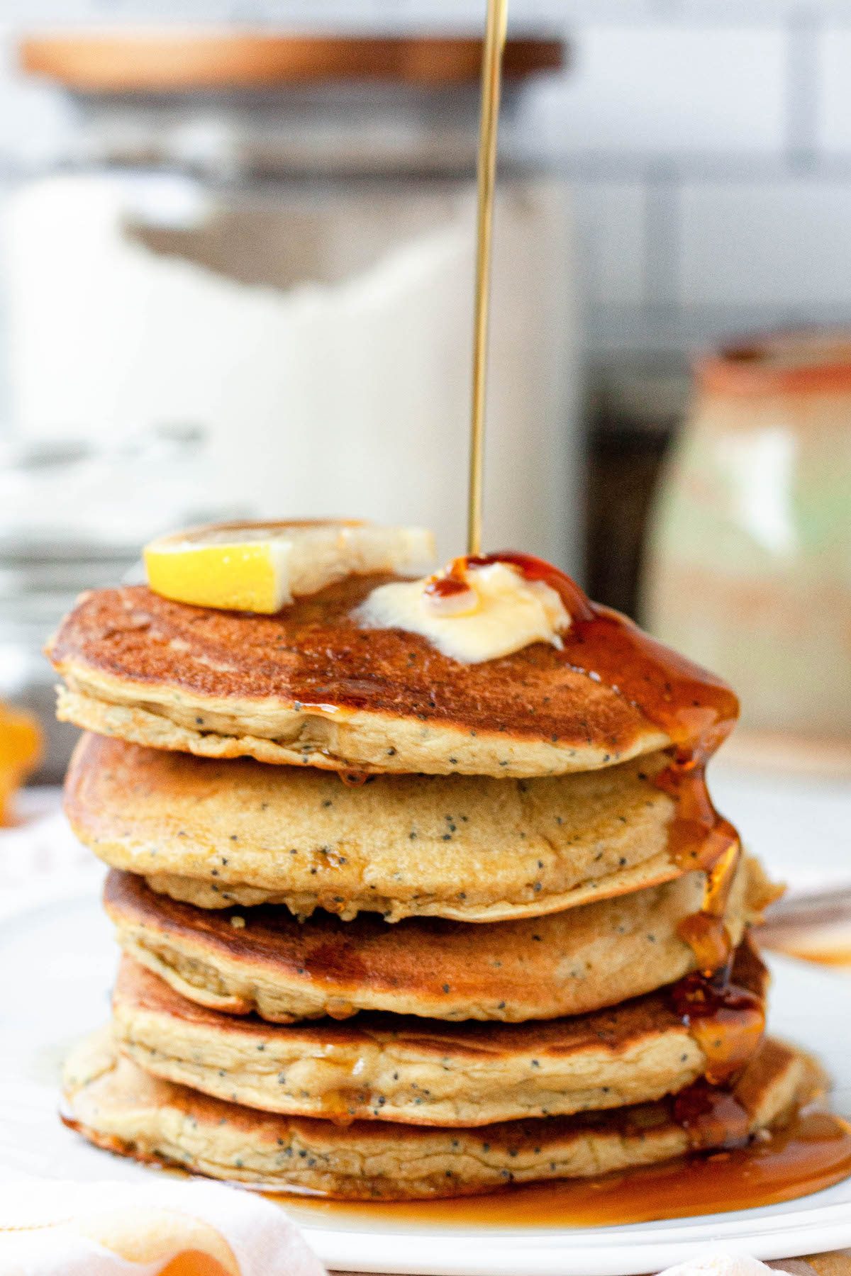 stack of vegan lemon poppy seed pancakes with maple syrup pour